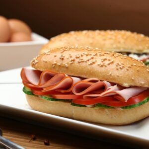 Tasty ham and vegetable sandwich on sesame bun with fresh ingredients served on a white plate.